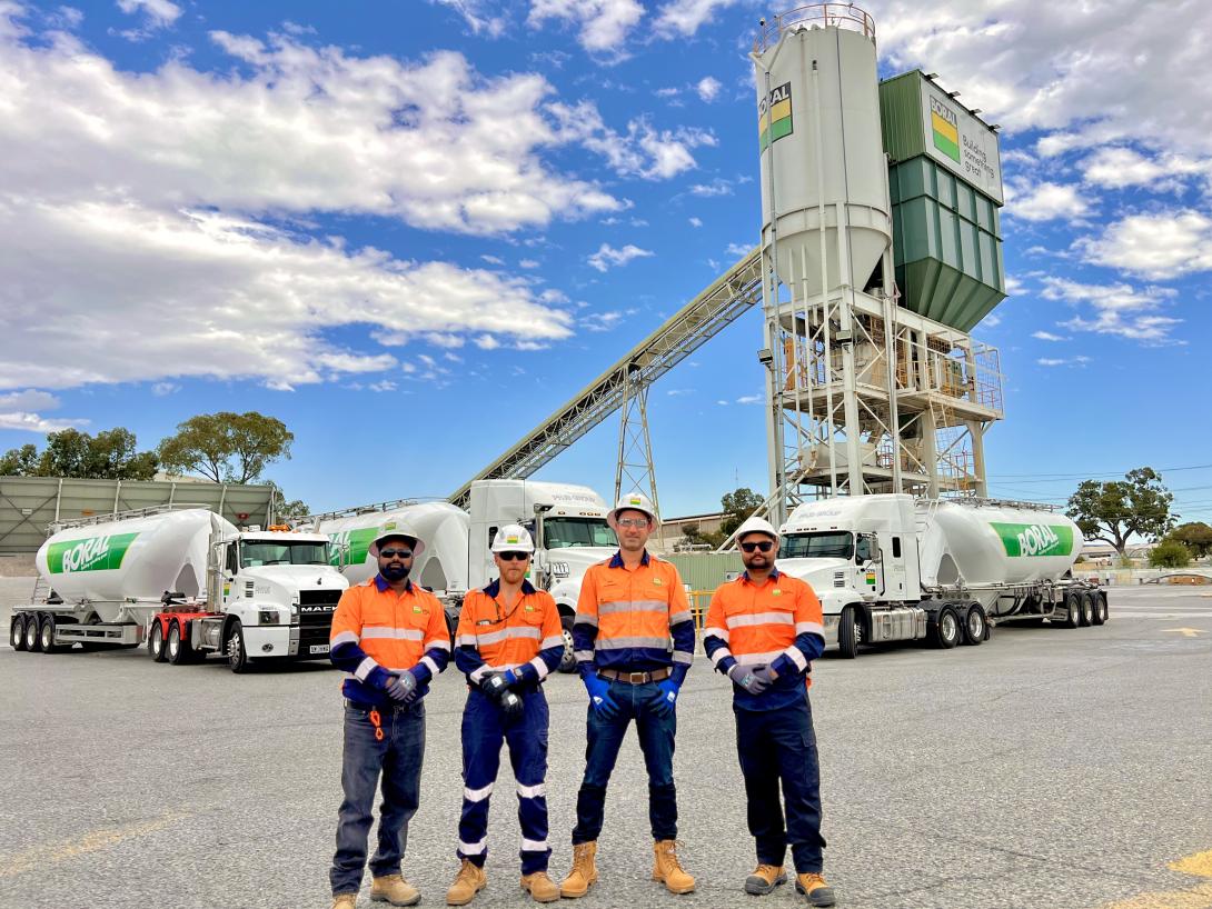 Group of staff standing in front of cement tanker trucks and a silo in the background